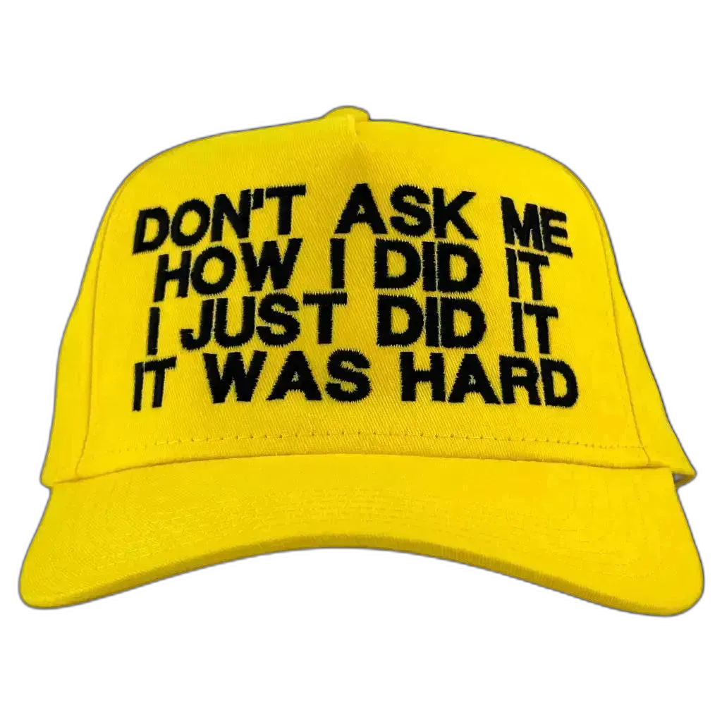 A bright yellow baseball cap with black embroidered text on the front that reads 'DON'T ASK ME HOW I DID IT I JUST DID IT IT WAS HARD'.