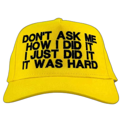 A bright yellow baseball cap with black embroidered text on the front that reads 'DON'T ASK ME HOW I DID IT I JUST DID IT IT WAS HARD'.